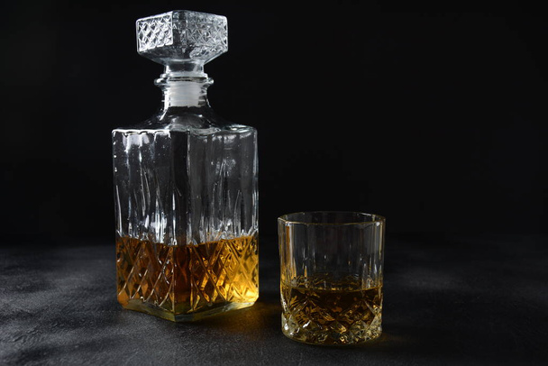 Glass of the whiskey with ice cubes and a square decanter on a black  background. - Photo, image