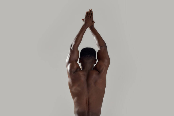 Rear view of muscular african american man with naked torso standing with his hands joined above his head. Swimmer about to dive isolated over grey background. Sports, swimming - 写真・画像