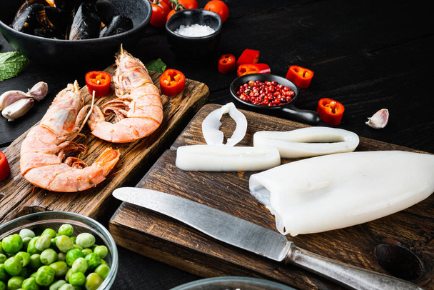 Spanish seafood paella ingredients, rice,prawns, mussels, peas on black wooden background, food photo. - Photo, Image