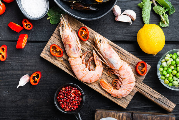 crevettes roi des fruits de mer sur panneau en bois avec des épices sur fond en bois noir, plat laïc, photo de la nourriture. - Photo, image