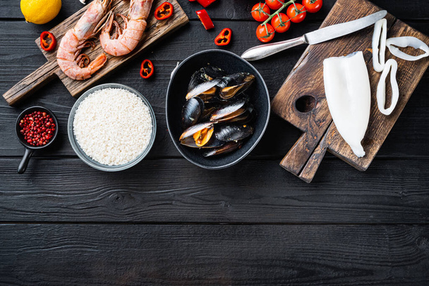 Meeresfrüchte für spanische Paella mit Gemüse und Gewürzen über schwarzem Holztisch, flache Liege mit Kopierraum, Food-Foto. - Foto, Bild