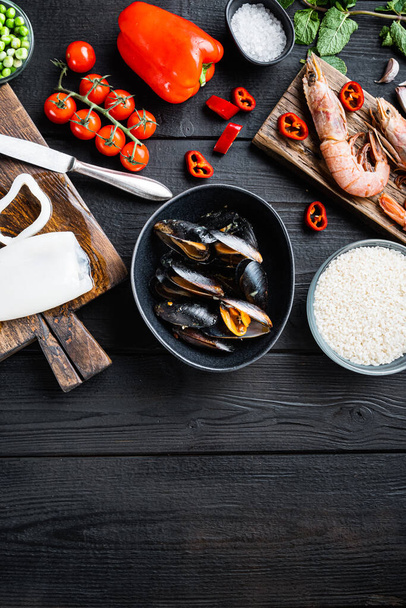 Frutti di mare per paella spagnola con verdure e spezie su fondo di legno nero, posa piatta con spazio copia, foto cibo. - Foto, immagini