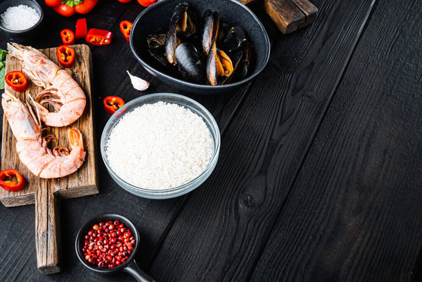 Ingredienti di pesce paella cruda su tavolo di legno nero con spazio per testo, foto cibo. - Foto, immagini