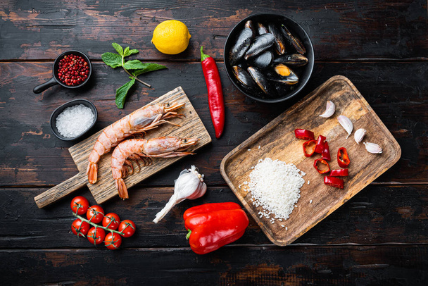 Typische Meeresfrüchte-Paella-Zutaten mit Reis, Miesmuscheln, Garnelen und Tintenfischen auf dunklem rustikalem Holzhintergrund, flache Lage, Food-Foto. - Foto, Bild