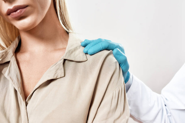 Навещаю врача. Обрезанный студийный снимок врача в синих стерильных перчатках, поддерживающего расстроенную пациентку, стоящую на сером фоне - Фото, изображение