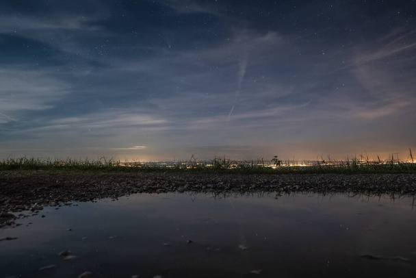 Cometa Neowise brilla a través de las nubes de algas, un agua en la carretera, detrás del horizonte es una vista de las ciudades en el país. - Foto, Imagen