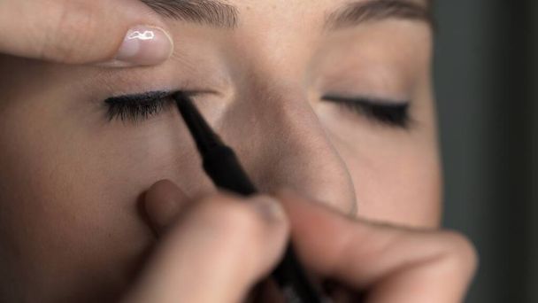 Makeup artist making professional make-up for young woman in beauty studio. Make up Artist applies black eyeliner to eyelid - Photo, Image