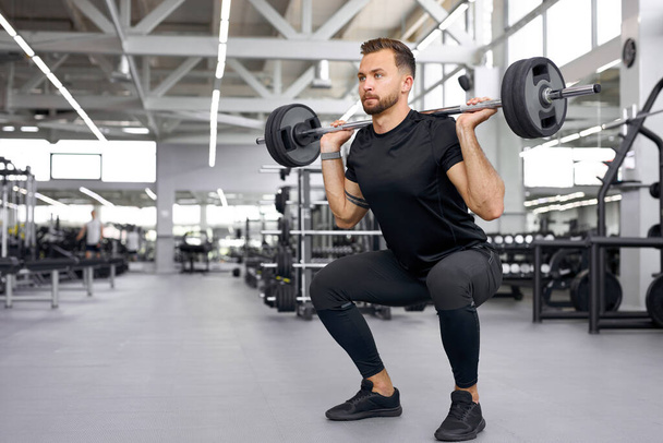sportsman squats and raises a large barbell in gym - Photo, Image
