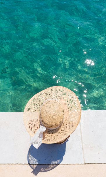 Mujer con sombrero de sol de verano grande relajante en el muelle por el mar turquesa claro. - Foto, Imagen