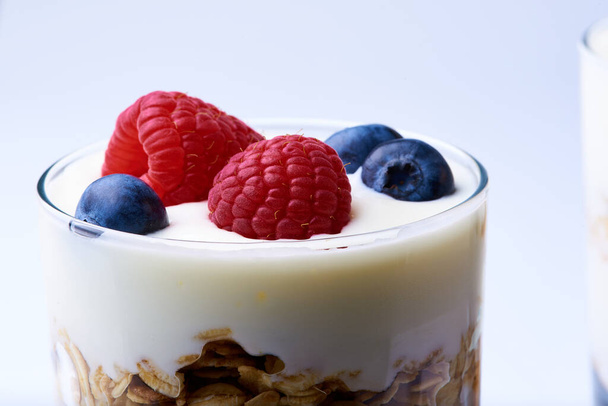 Egy pohár granola, joghurt, málna és áfonya fehér alapon - Fotó, kép