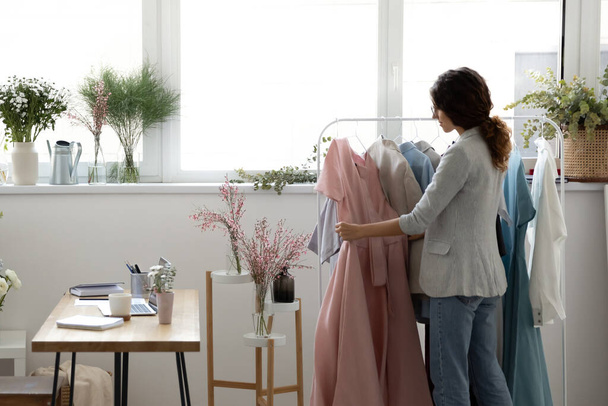 Concentrated young businesswoman arranging newly crafted female clothing collection. - 写真・画像
