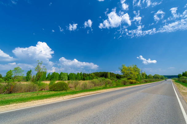 spring photo taken with a wide-angle lens, local highway, bright green trees, clouds in the blue sky - Photo, Image
