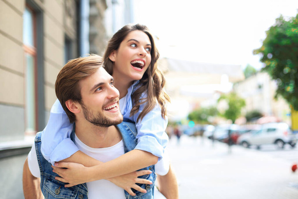 Handsome young man carrying young attractive woman on shoulders while spending time together outdoors - Photo, image