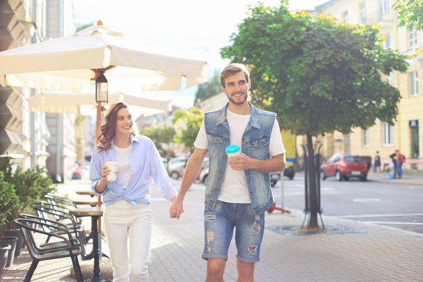 Image of lovely happy couple in summer clothes smiling and holding hands together while walking through city street - Foto, imagen