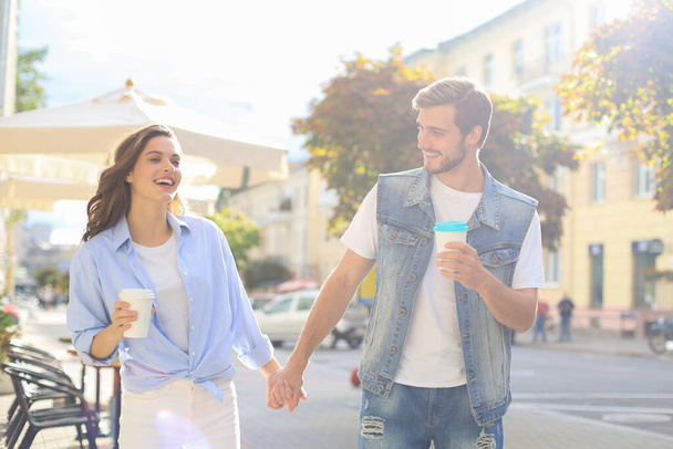 Image of lovely happy couple in summer clothes smiling and holding hands together while walking through city street - Φωτογραφία, εικόνα