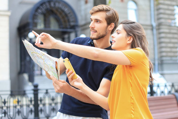 Beautiful young couple holding a map and smiling while standing outdoors - Φωτογραφία, εικόνα