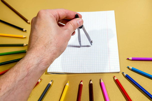 A man's hand with a compass draws on a white notebook sheet - Zdjęcie, obraz
