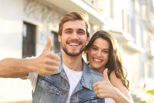 Image of a happy smiling cheerful young couple outdoors take a selfie by camera showing thumbs up - Foto, immagini