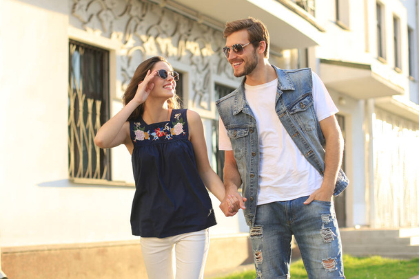 Image of lovely happy couple in summer clothes smiling and holding hands together while walking through city street - Foto, Bild
