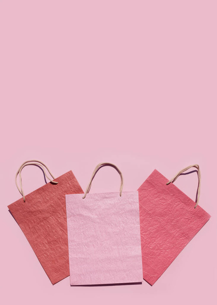 ピンクの背景にカラフルなテクスチャペーパーショッピングバッグ。最小限のファッションショッピングオンラインコンセプト。コピースペース、トップビュー、フラットレイアウト。モックアップ. - 写真・画像