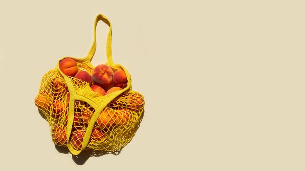Ripe peaches in a mesh bag or string bag on light yellow background. Flat lay. Zero waste. Top view. - 写真・画像