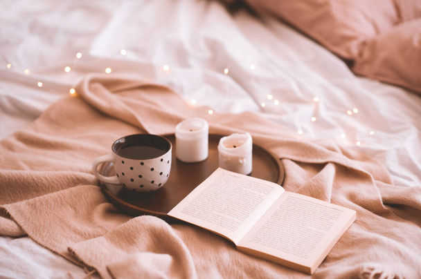 Cup of coffee with open book and candles in bed closeup. Autumn season. Good morning. Selective focus.  - 写真・画像