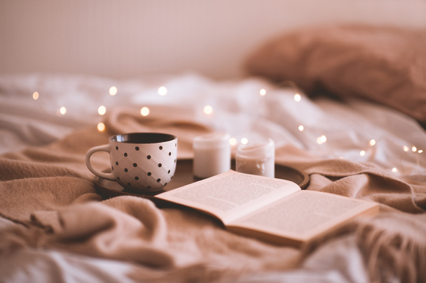 Açık kitaplı bir fincan kahve ve yatakta mumlar. Sonbahar sezonu. İyi sabahlar. Seçici odak.  - Fotoğraf, Görsel
