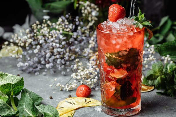 Strawberry Mojito. Cold summer mojito cocktail with strawberries, mint, lemon and ice in a glass on a table. on a dark background. - Zdjęcie, obraz