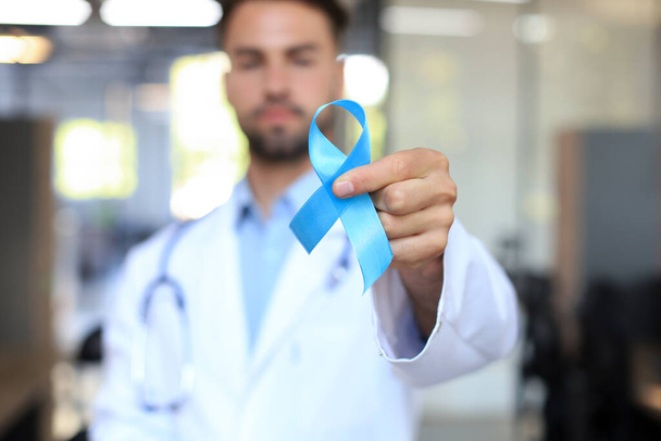 Doctor hand with blue prostate cancer awareness ribbon. Medicine oncology closeup sky symbol - Photo, Image