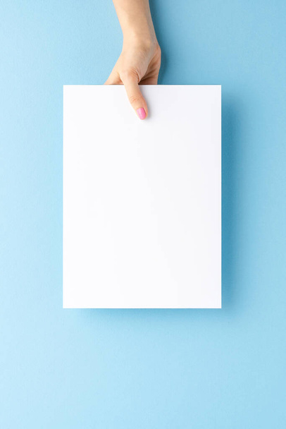 Young woman hand holding blank paper sheet on blue background. Mockup - Zdjęcie, obraz