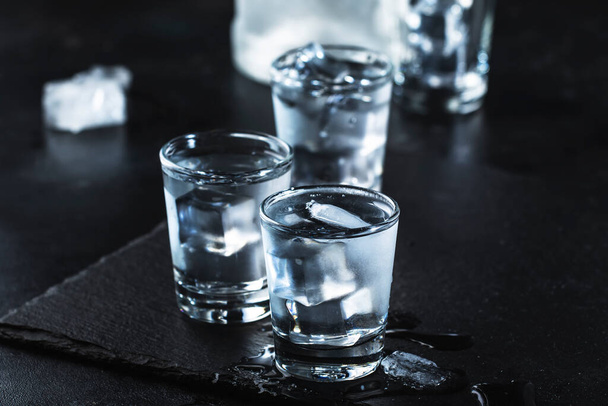 Vodka in shot glasses on black stone background, iced strong drink in misted glass - Foto, Imagen