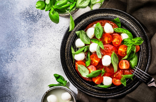 Tasty caprese salad with ripe red tomatoes and mozzarella cheese with fresh green basil leaves. Italian food. Top view - Foto, imagen