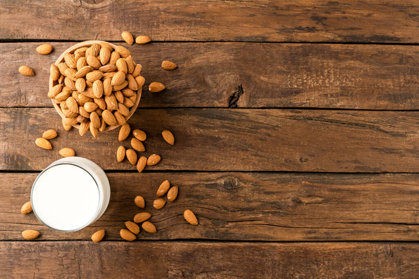 Glass of almond milk on rustic wooden background with almonds and copyspace. Top view - 写真・画像