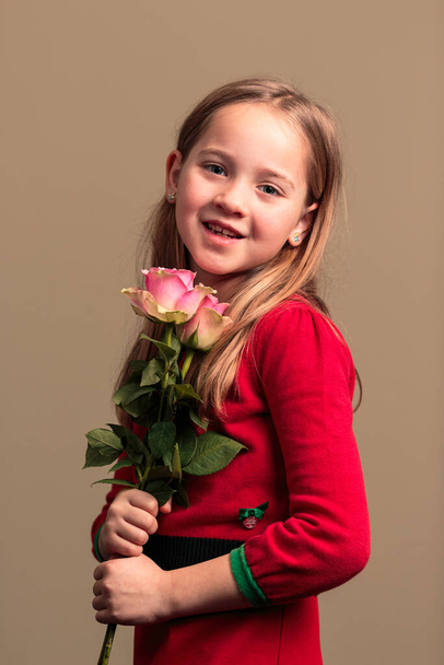 Jovem bonita menina de 8 anos vestindo um vestido vermelho segurando flores isoladas no fundo de cor laranja - Foto, Imagem