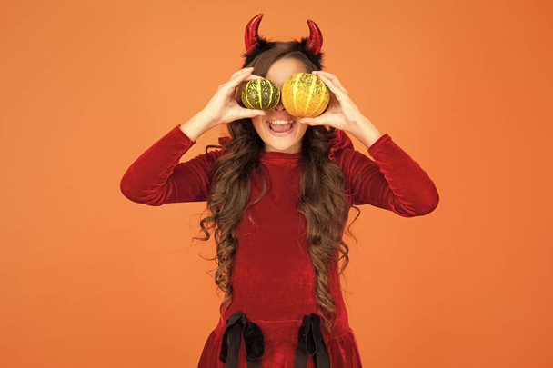 Playful imp. Girl with horns play with pumpkins. Happy holidays. Cute child celebrate Halloween. Autumn holidays. Pumpkins traditional attribute of fall holidays. Having fun. Decorations for holidays - Foto, Bild