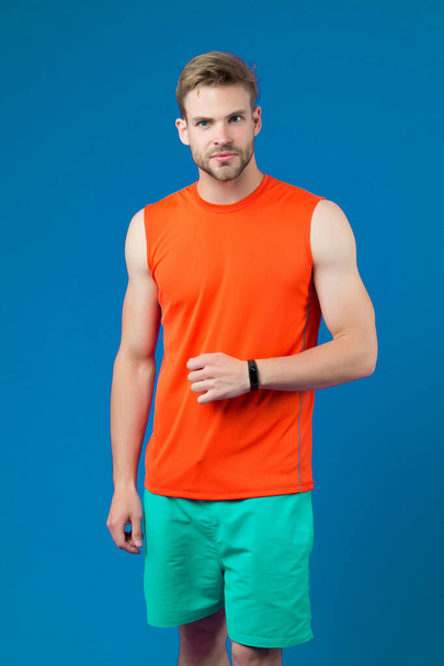 Man with sport smartwatch on violet wall. Sportsman in orange vest and blue shorts. Fashion accessory for training and workout. New technology for healthy lifestyle. Sport or fitness and wellness - Foto, Imagem