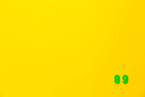 A green plastic toy number eighty-nine is located in the lower right corner on a yellow background. - Photo, Image