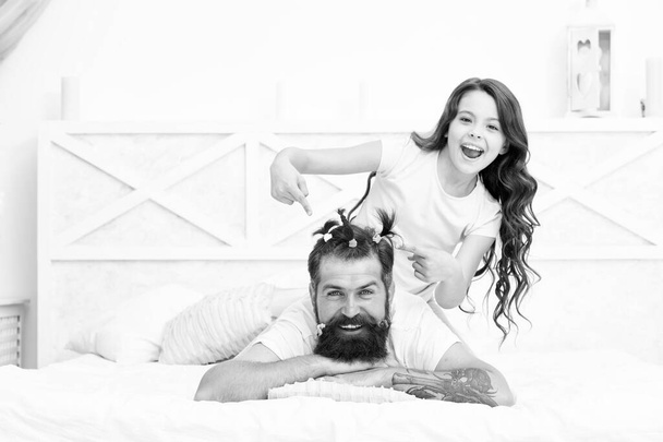 Relaxing in bedroom. Affection and support. Stay home and have fun. Family leisure concept. Girl making hairdo for dad. Quarantine with children. Happy family. Pajamas party. Happy childhood - Foto, Imagen