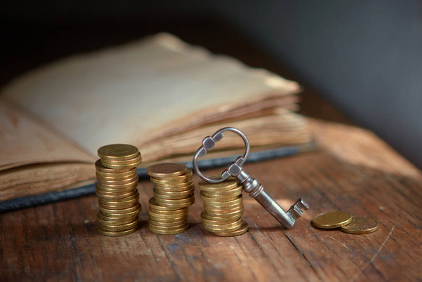 An old beautiful old key, a stack of gold coins, an old book. Business start-up, investment, treasure hunting, or the concept of the key to success - Valokuva, kuva