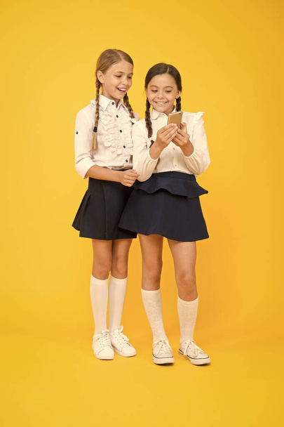 cheerful classmates with smartphone. little girls in school uniform. back to school. educational blog. new technology in education. knowledge day. internet surfing with 4g. kids study online - Фото, изображение