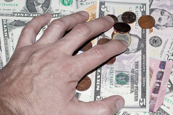 το χέρι τοποθετείται πάνω από αμερικανικά δολάρια, ευρώ και μεταλλικά νομίσματα - Φωτογραφία, εικόνα