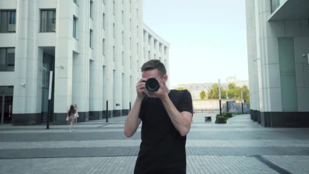 Profesyonel fotoğrafçı seni vurur. Başla. Genç adam şehirde yürürken seni profesyonel kameraya alır. Fotoğrafçı modern mimariyle şehirde dolaşıyor. - Video, Çekim