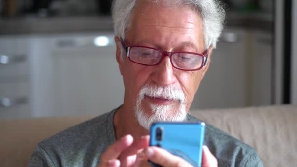 Senior ηλικιωμένος 70s άνθρωπος χρησιμοποιώντας έξυπνο τηλέφωνο καλώντας σε απευθείας σύνδεση κοιτάζοντας την οθόνη χαλαρώνοντας στο σπίτι  - Πλάνα, βίντεο