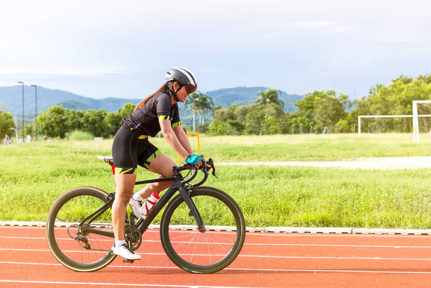asiático joven mujer atletas ciclismo en una pista de carreras intensamente y felizmente en campo de deportes al aire libre en día brillante - Foto, Imagen