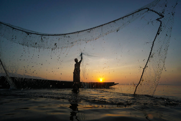 rybak rzucając sieci rybackie do cathch ryb w jeziorze hte rano - Zdjęcie, obraz