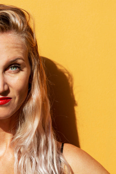 Smiling blonde on a yellow background. Half face, space for text. Bright sunlight. Vertical. - Foto, Bild