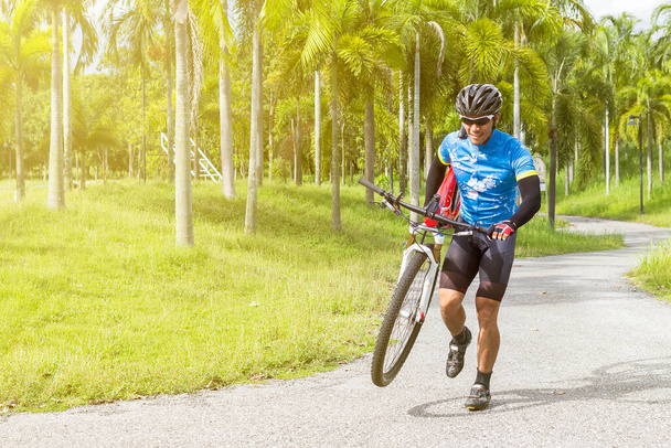 Asyalı sporcular bahçede güneş ışığıyla koşup bisiklet taşıyorlar. - Fotoğraf, Görsel