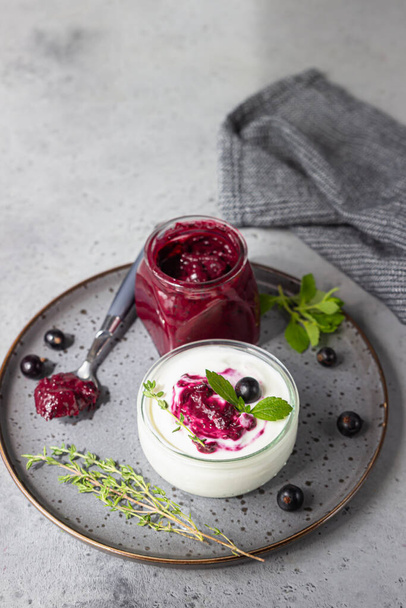 Jar of delicious homemade black currant curd, custard or jam with natural yogurt and fresh berries on grey concrete background. Healthy breakfast. - Zdjęcie, obraz