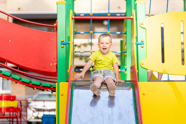 szczęśliwy chłopiec bawiący się na placu zabaw, chłopiec toczący się ze wzgórza, styl życia dzieci - Zdjęcie, obraz