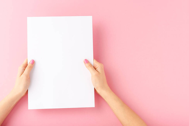 Female hands holding blank white paper sheet on pink background. Mock up - Zdjęcie, obraz